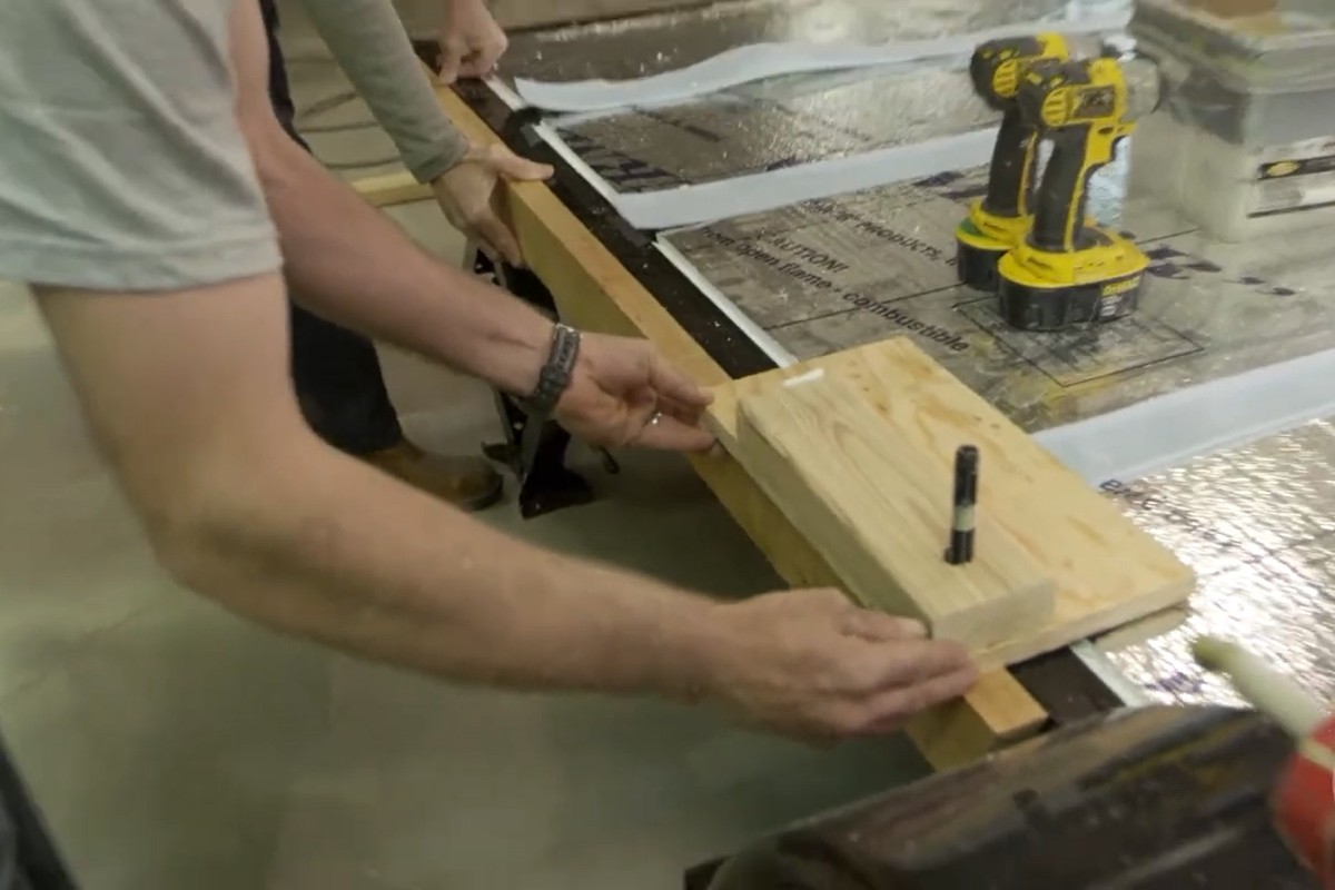 Two people assembling a wooden structure with a drill on a reflective surface, securing pieces with a screwdriver.